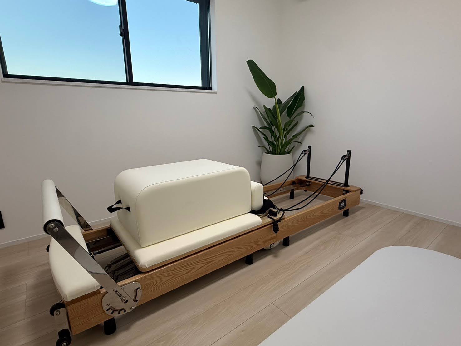 OB PILATESのスタジオ内観 — 窓からの光が入る部屋にリフォーマーとマット